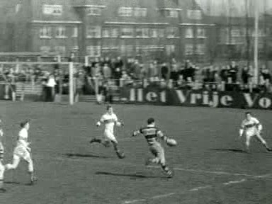 Zwart-witbeeld uit een Polygoon-journaal waarop een AAC-rugbyspeler in een shirt met brede banen met de bal naar drie verdedigers van Bank of England loopt in Amsterdam in april 1955.