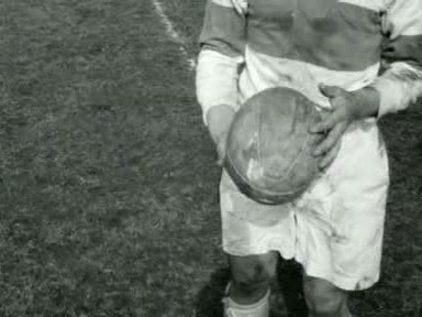 Zwart-witte close-up van een AAC-rugbyspeler in een shirt met brede banen, met een versleten leren rugbybal in de handen, Amsterdam april 1955.