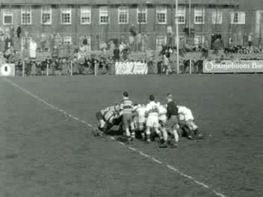 Zwart-wit overzicht van AAC in shirts met brede banen en Bank of England in lichte shirts in een scrum in Amsterdam, april 1955, met toeschouwers achter de verre zijlijn.
