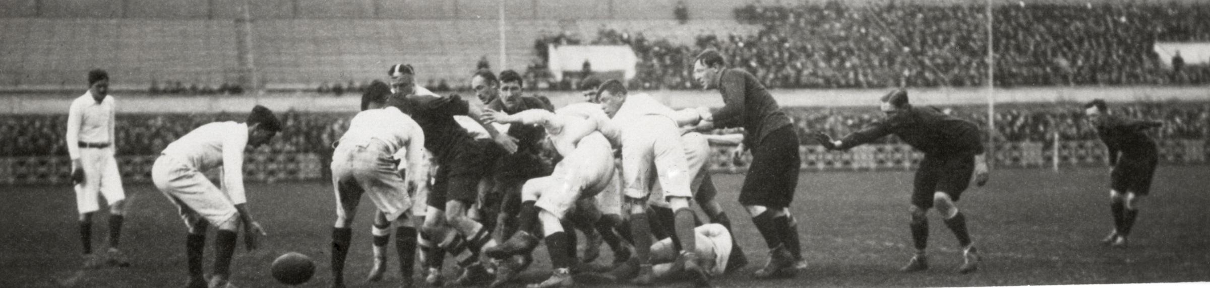 Brede zwart-witfoto uit 1918 van twee teams Britse geïnterneerden in een rugby-scrum in Stadion Amsterdam, met publiek op de achtergrond.