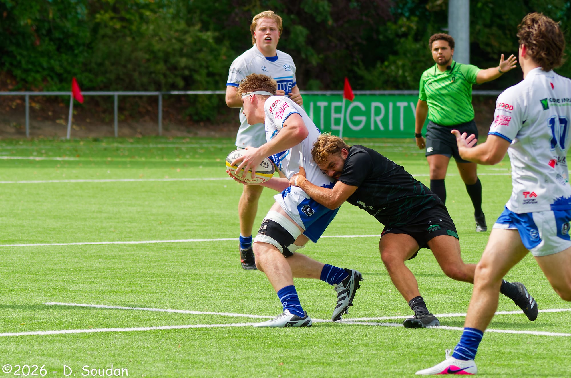 Een AAC-speler in wit-blauw wedstrijdtenue in een tackle tegen Royal Kituro