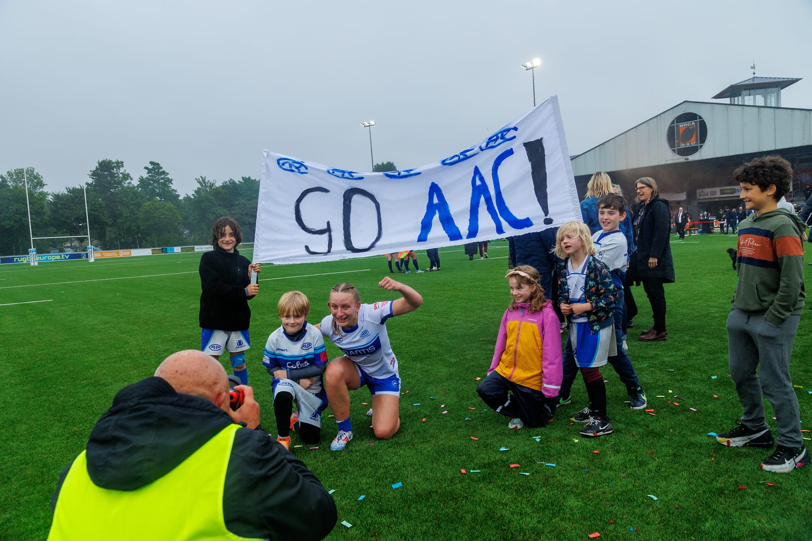 AAC-speelster knielt met kinderen die een spandoek met Go AAC vasthouden na het eindsignaal