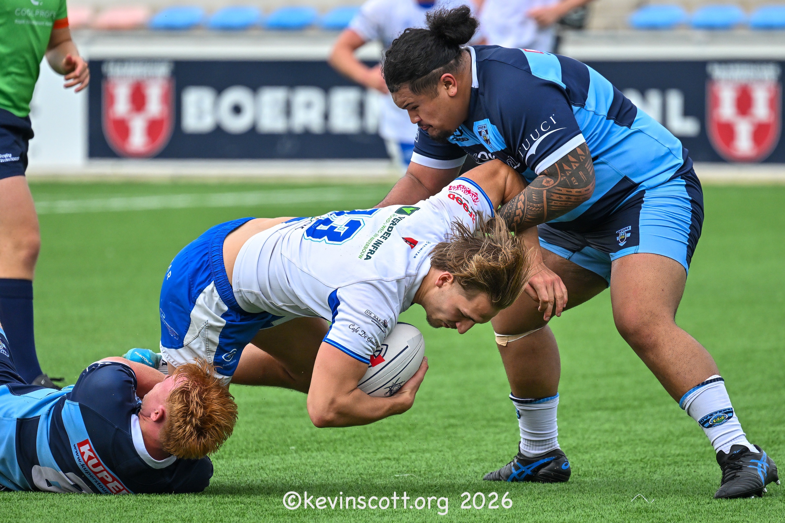 Een AAC-speler in wit-blauw tenue stapt met de bal tegen RFC Oisterwijk Oysters